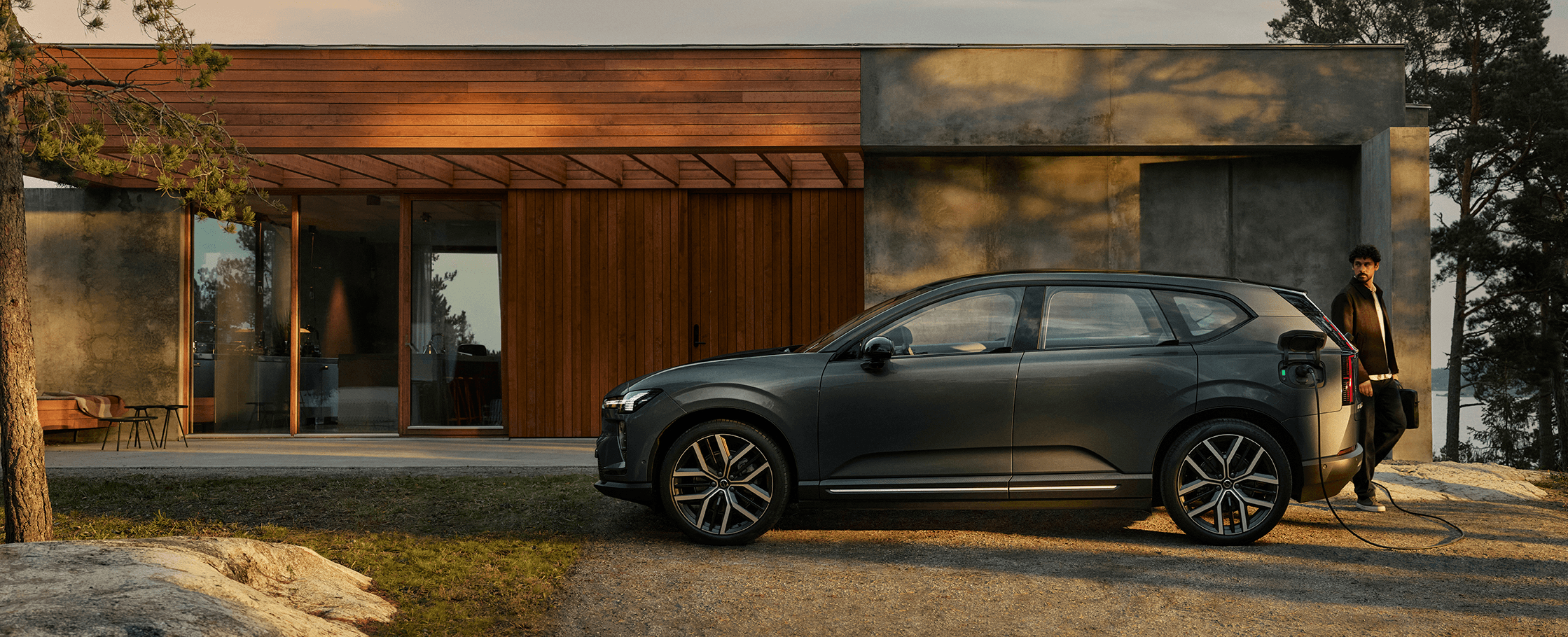 Volvo EX60 beim Laden vor einem modernen Holzhaus